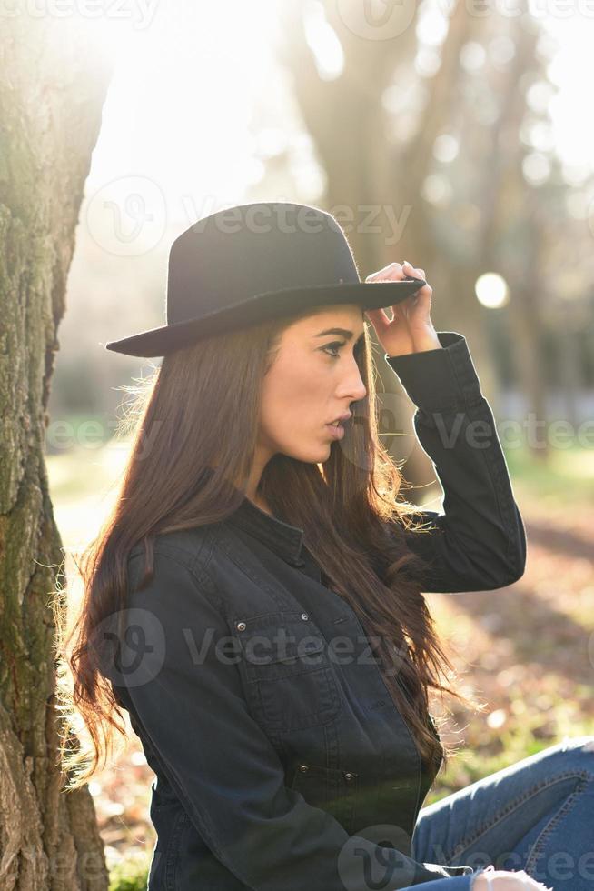 Thoughtful woman sitting alone outdoors wearing hat photo