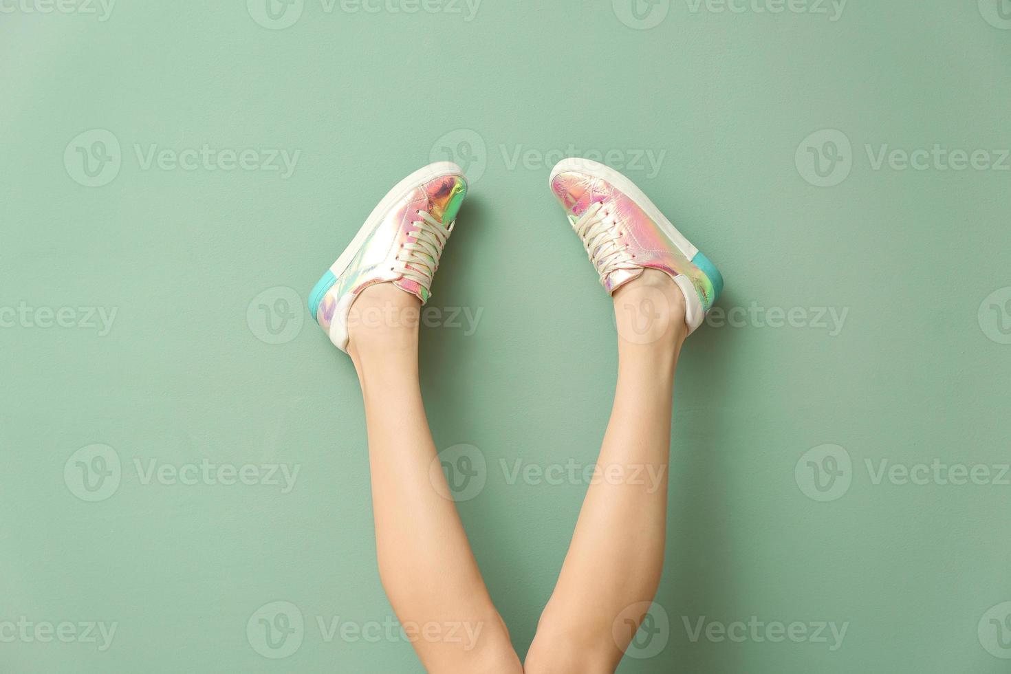 Legs of young woman in stylish casual shoes on color background photo