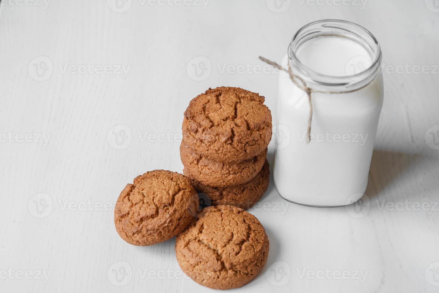 Leche en un frasco de vidrio y galletas de avena sobre una mesa blanca foto