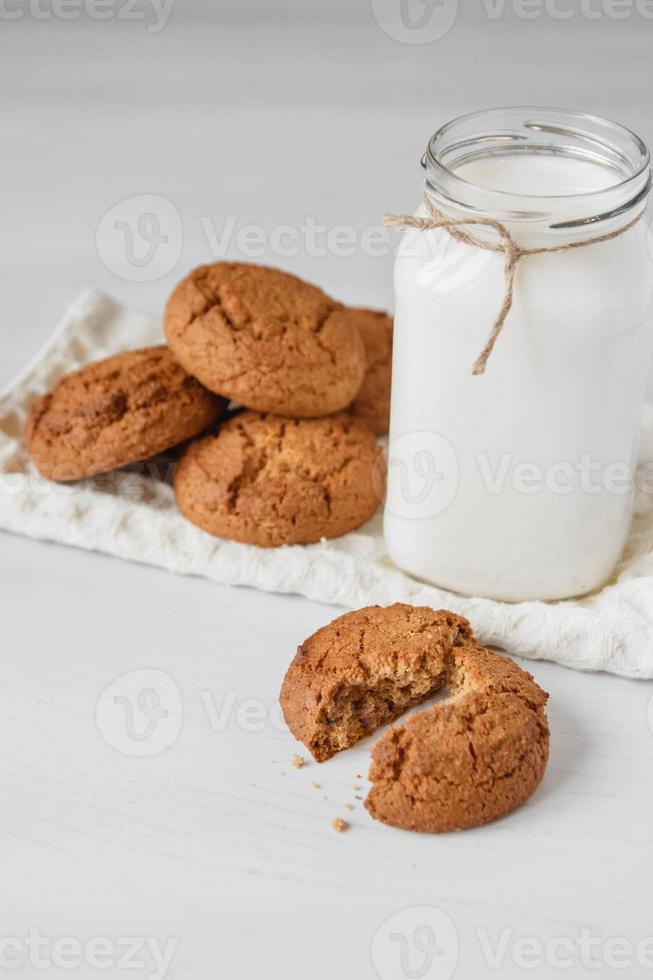 Leche en tarro de cristal y galletas de avena cerca de la servilleta en el cuadro blanco foto