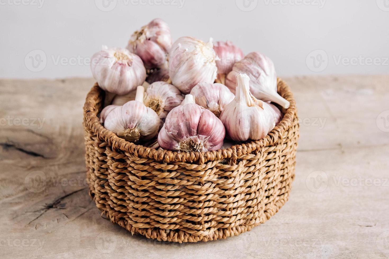 Garlic in a wicker basket on a wooden table background photo