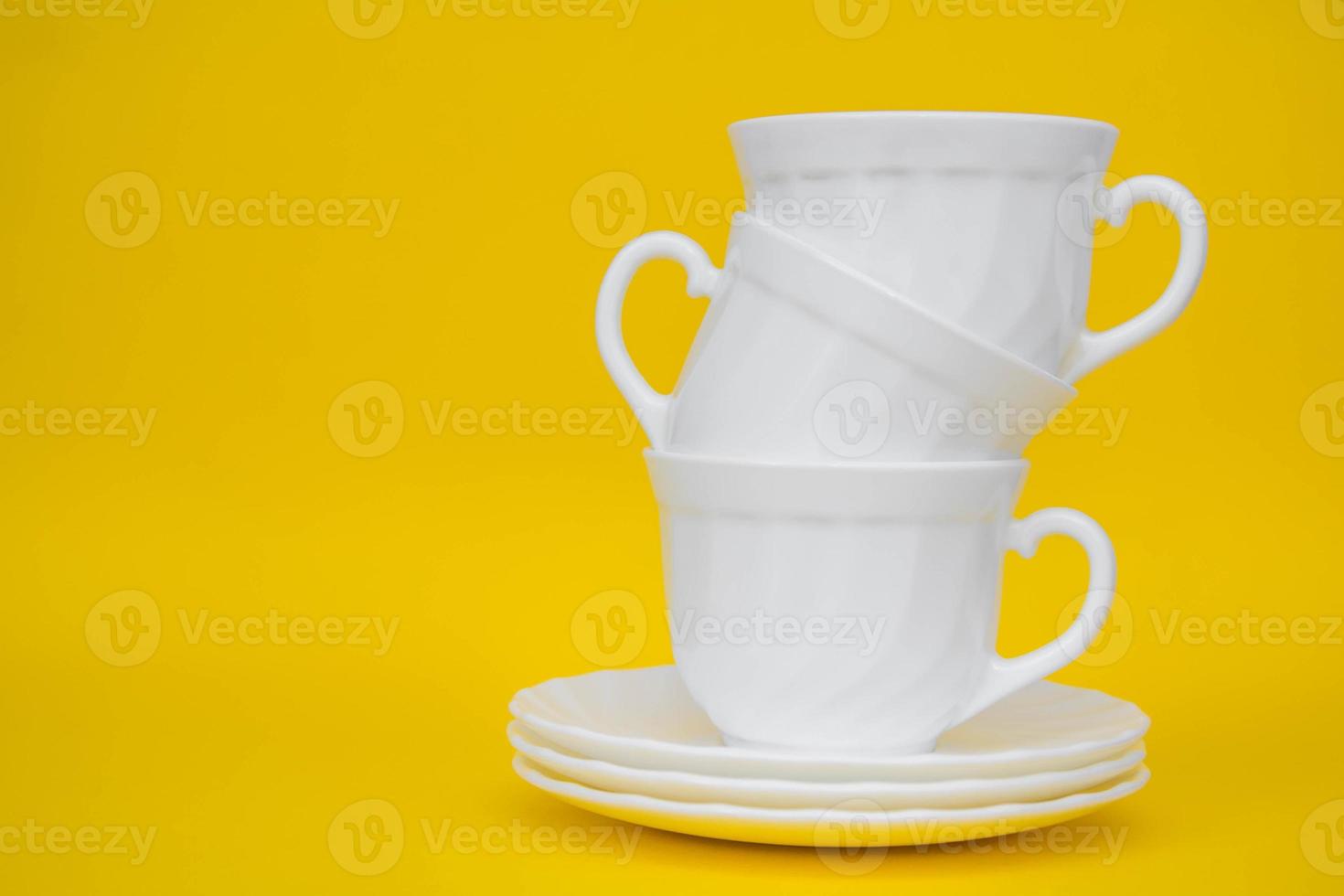 White ceramic cups with saucers folded pyramid on yellow background photo