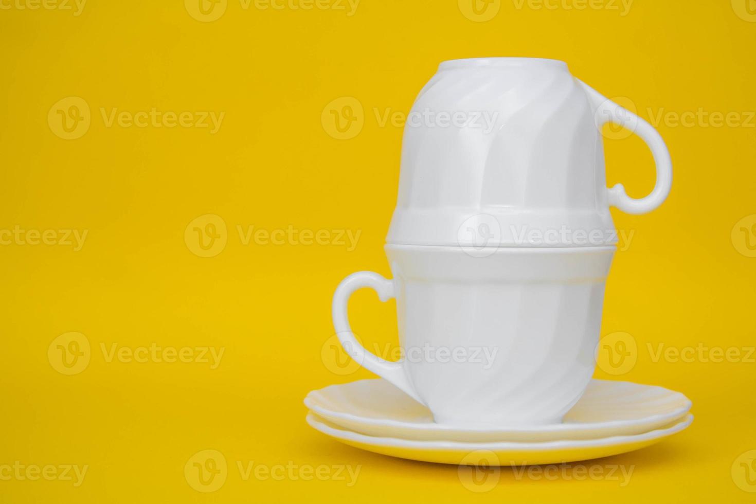 Tazas de cerámica blanca con platillos sobre fondo amarillo foto