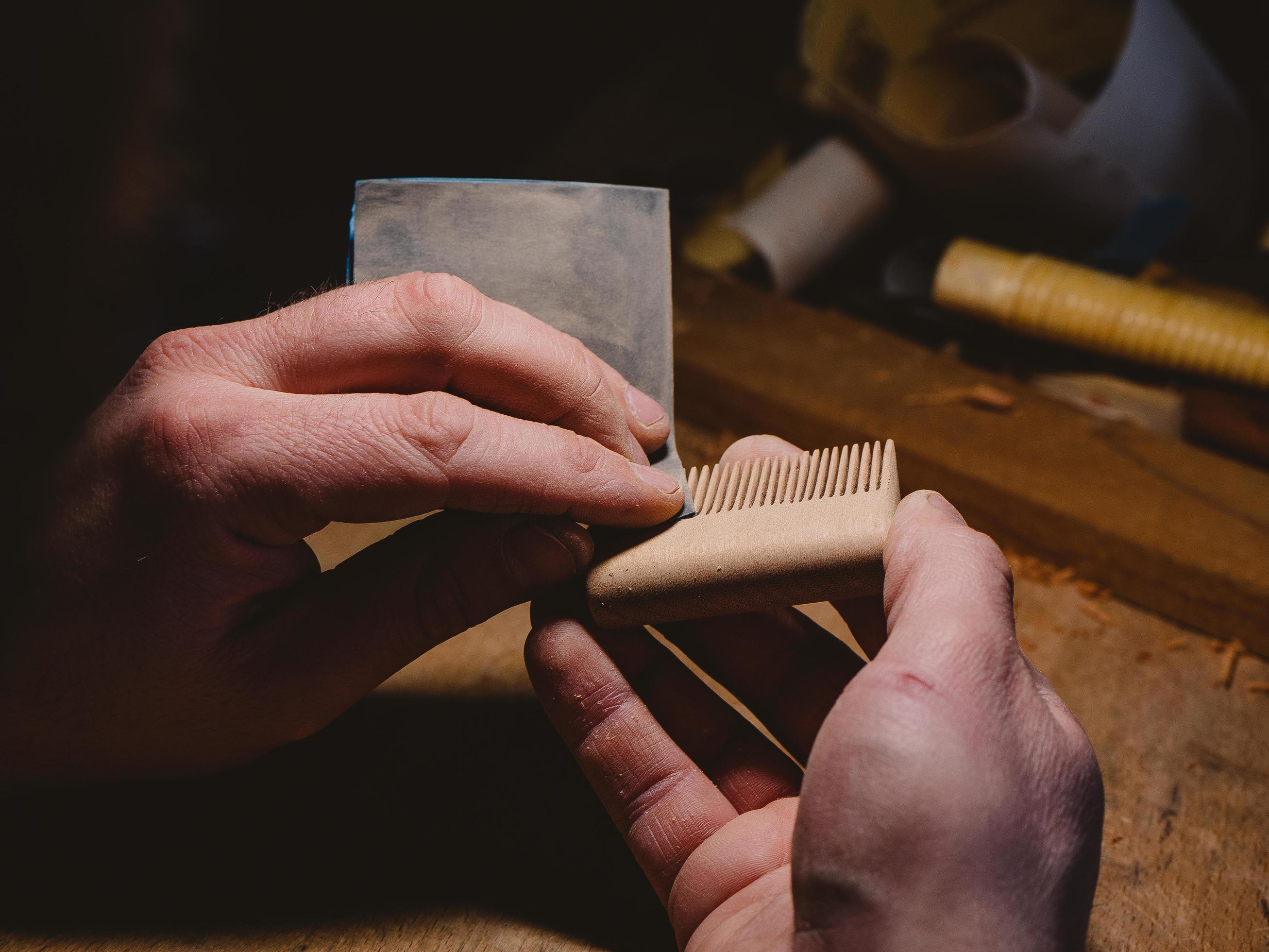 craftsman sanding a handmade beard comb with sanding paper. beard and