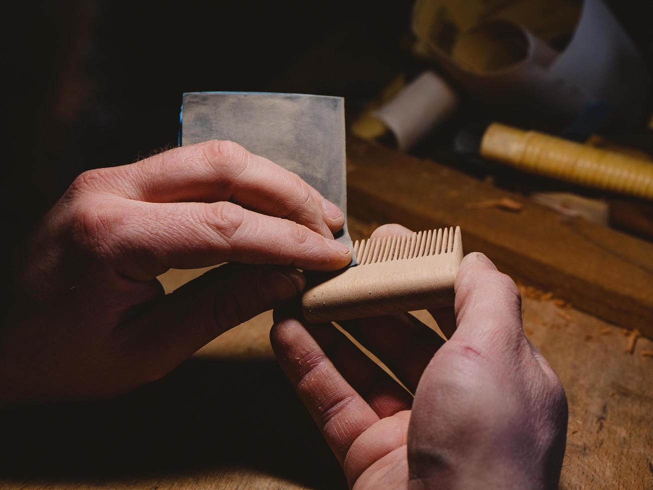 craftsman sanding a handmade beard comb with sanding paper. beard and mustache concept. beard accessories . wooden beard comb photo