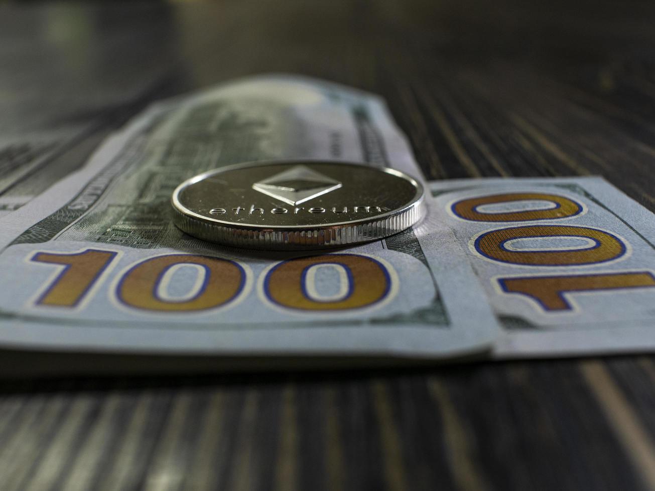 Silver Ethereum on US dollars. Digital currency close-up on a wooden background.Real coins of bitcoin on banknotes of one hundred dollars photo