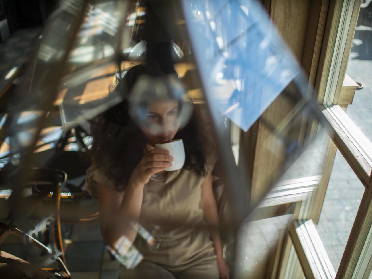 attractive girl with curly hair sits in a cafe at the table and drinks coffee photo