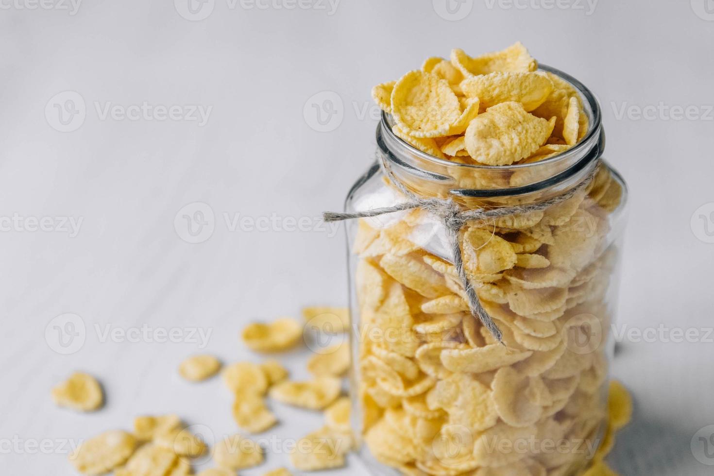 Copos de maíz en un frasco de vidrio sobre la superficie de madera blanca foto