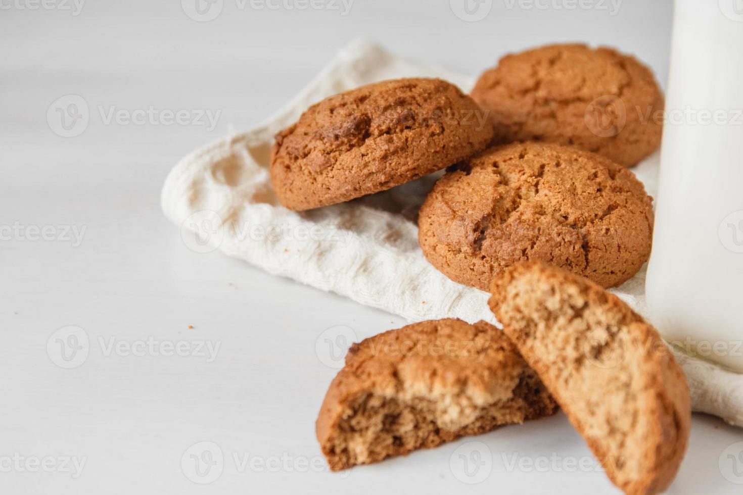 Milk in glass jar and oatmeal cookies near napkin on white table photo