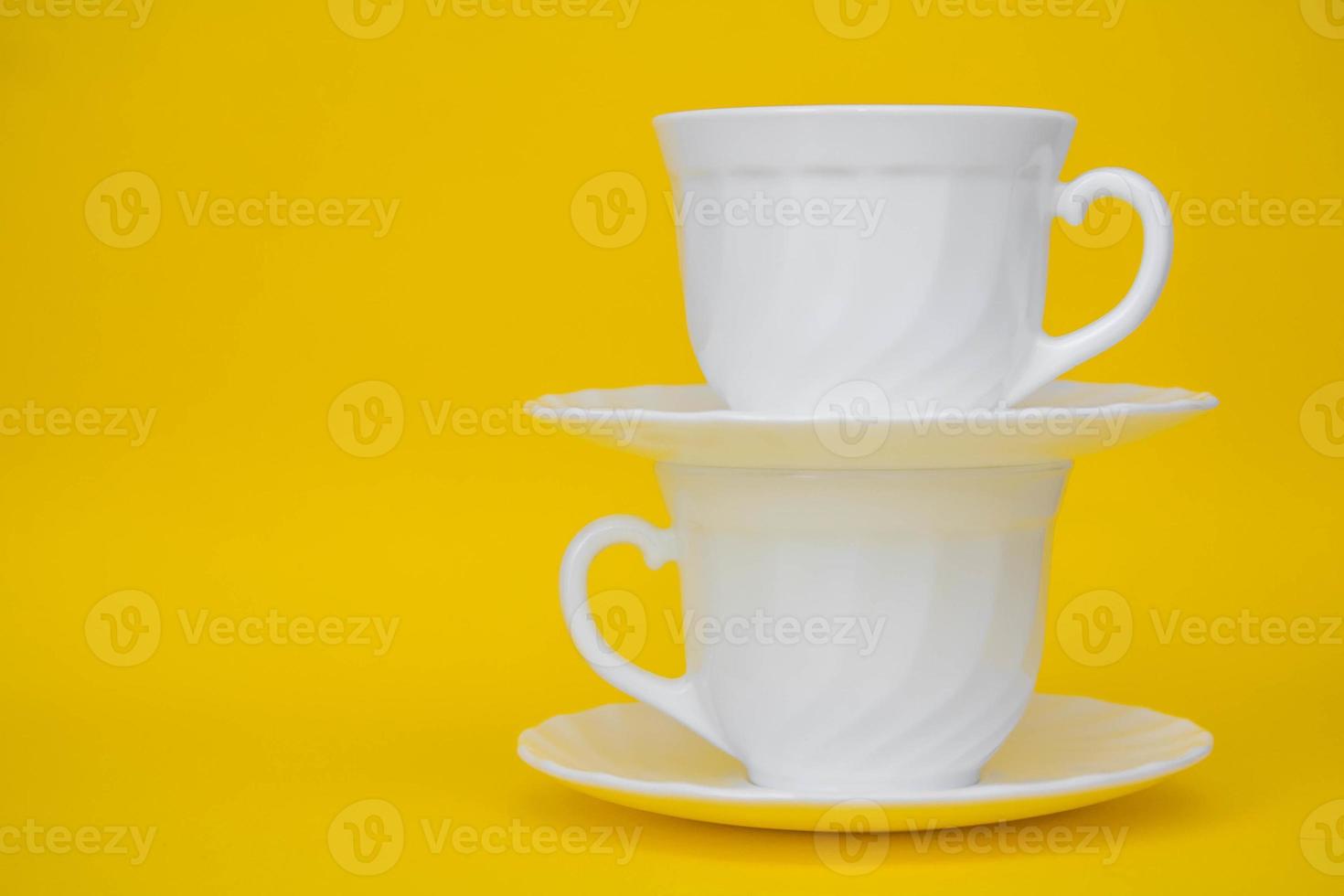 Tazas de cerámica blanca con platillos sobre fondo amarillo foto