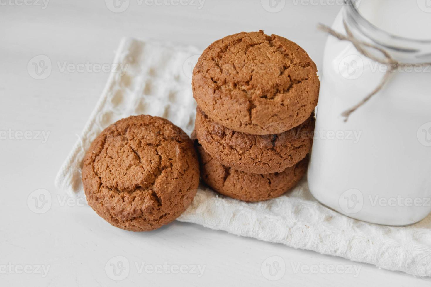 Leche en tarro de cristal y galletas de avena cerca de la servilleta en el cuadro blanco foto