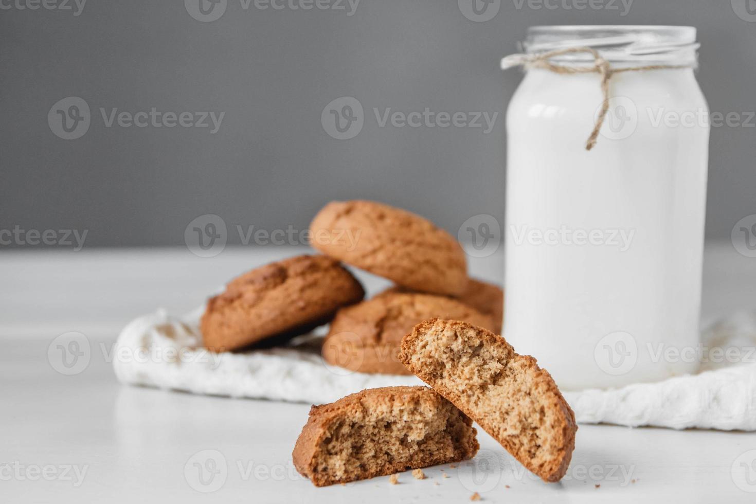 Milk in glass jar and oatmeal cookies near napkin on white table background photo