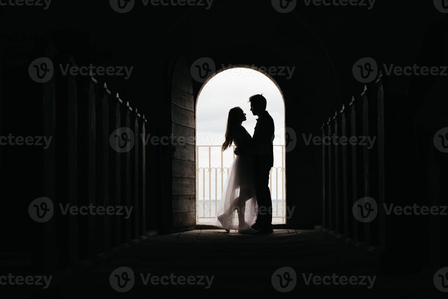 Silhouette of loving couple hugging while standing in doorway on black background photo