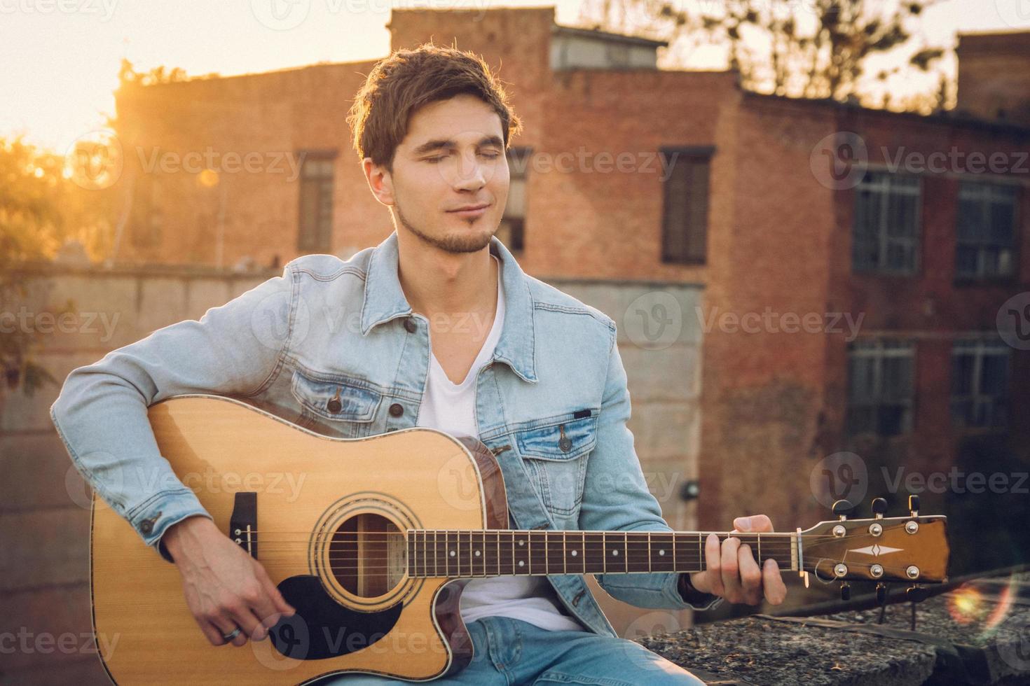 Joven tocando la guitarra en la ciudad sobre fondo de rayos de sol foto