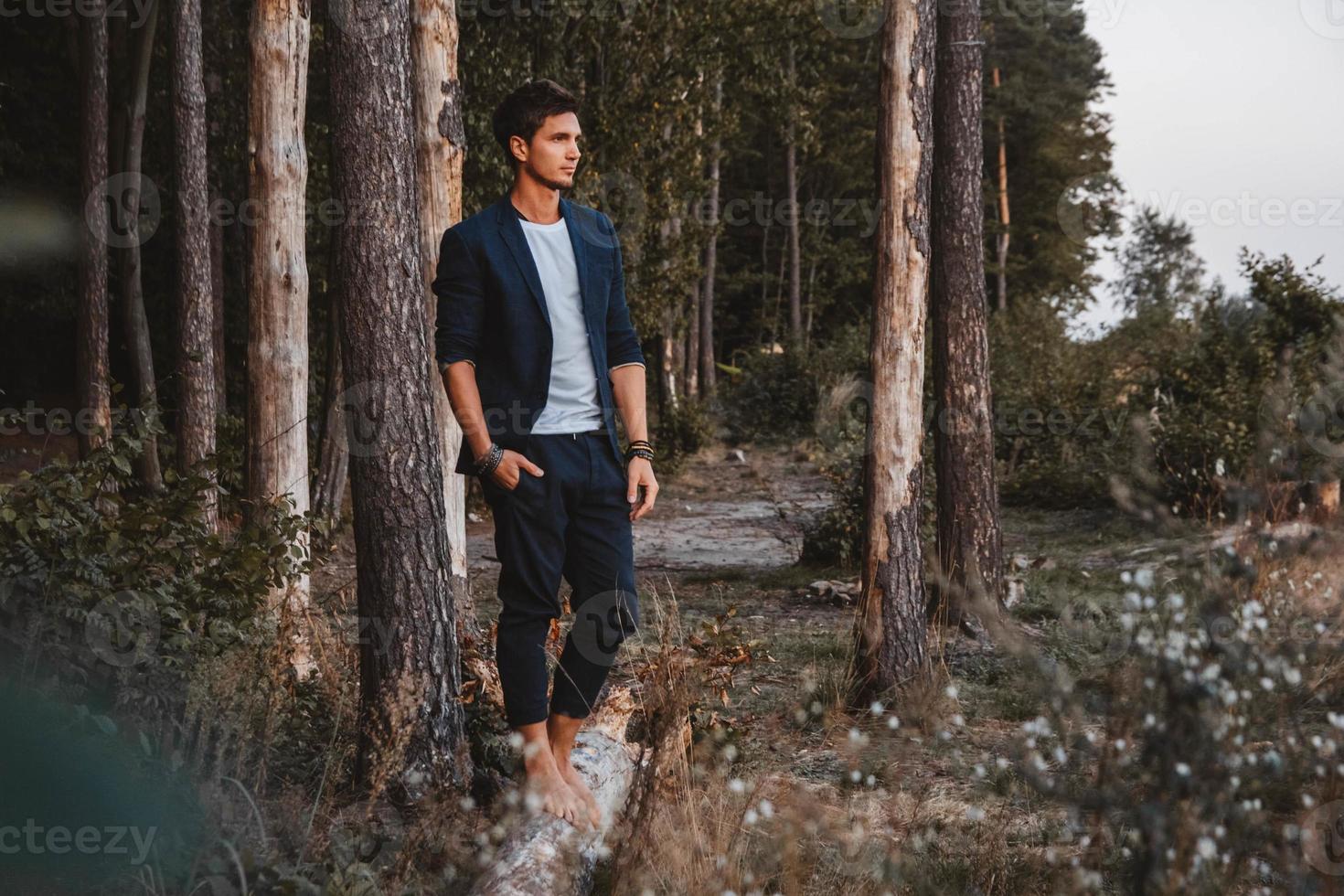 El hombre posando al aire libre en el bosque está descalzo sobre un tronco, vistiendo chaqueta de cuadros foto