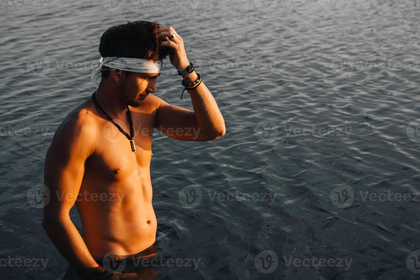 Man with perfect muscular stands in the water at sunset photo