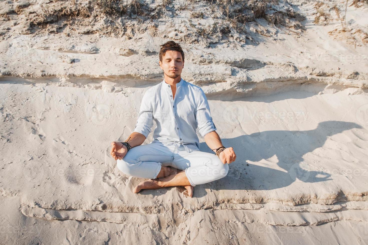 El hombre se sienta en pose de meditación en la playa de arena foto