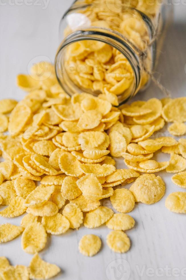 Corn flakes in a glass jar on white wooden surface photo