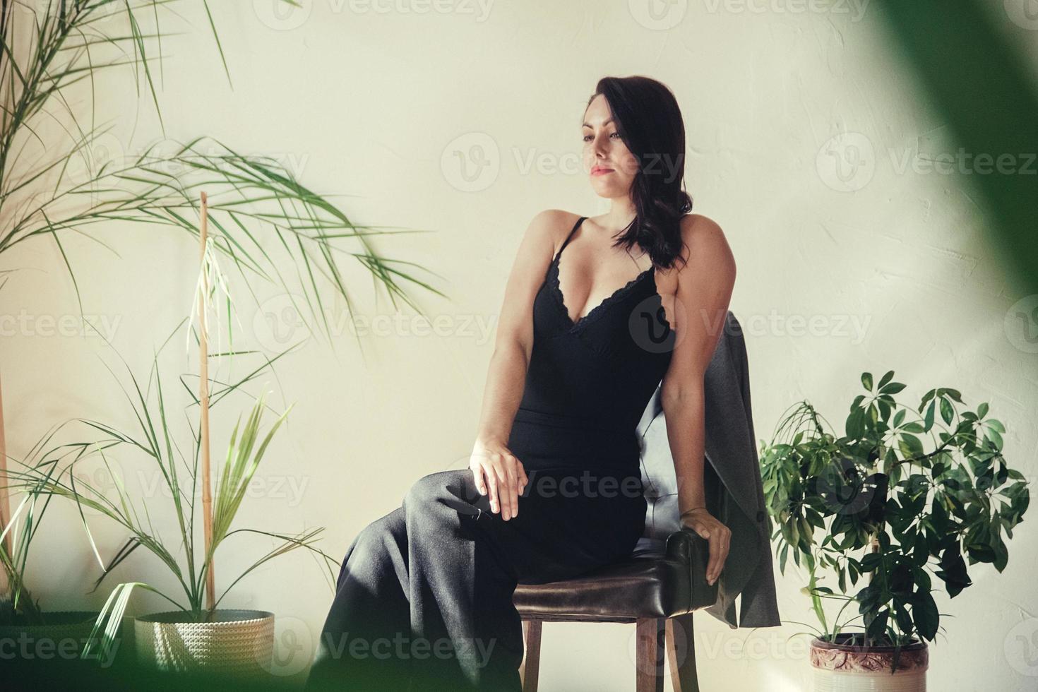Mujer vestida con ropa negra se sienta en una silla en el interior de estilo loft foto