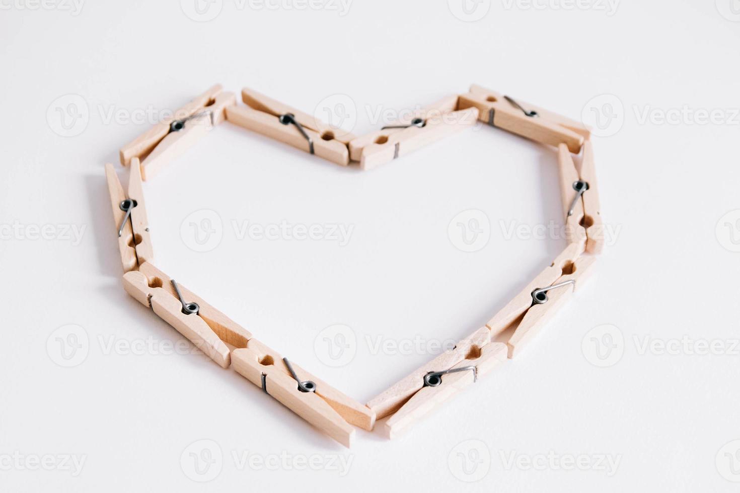 Wooden clothespins on white background which are folded in form of heart icon photo