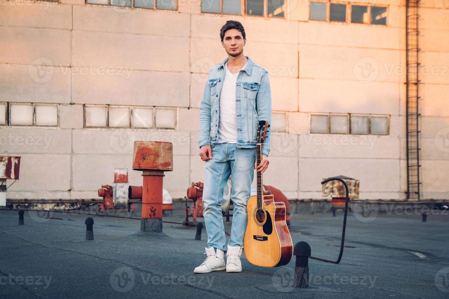 Joven sosteniendo la guitarra en la ciudad sobre los rayos del sol antecedentes foto