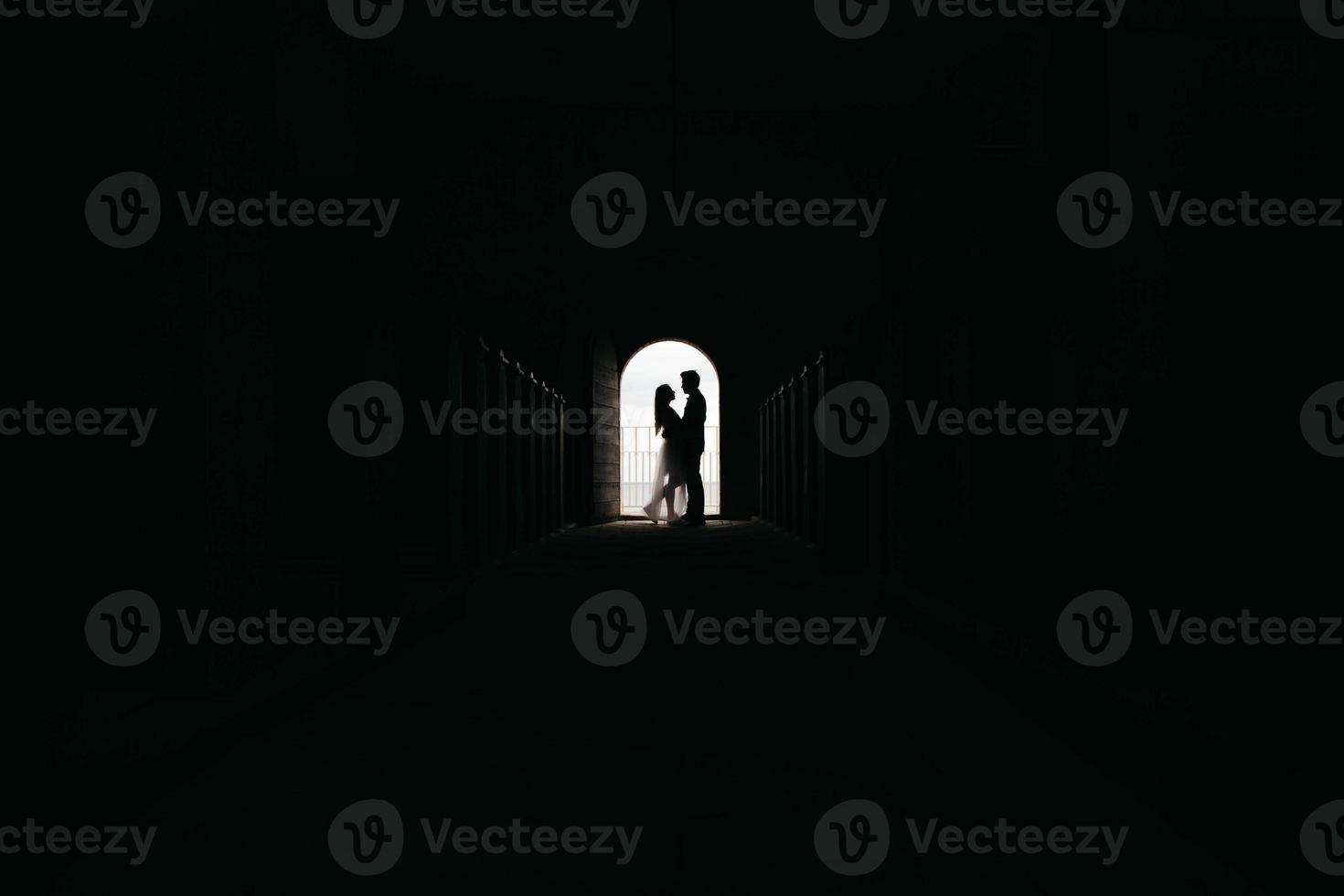 Silhouette of loving couple hugging while standing in doorway on black background photo