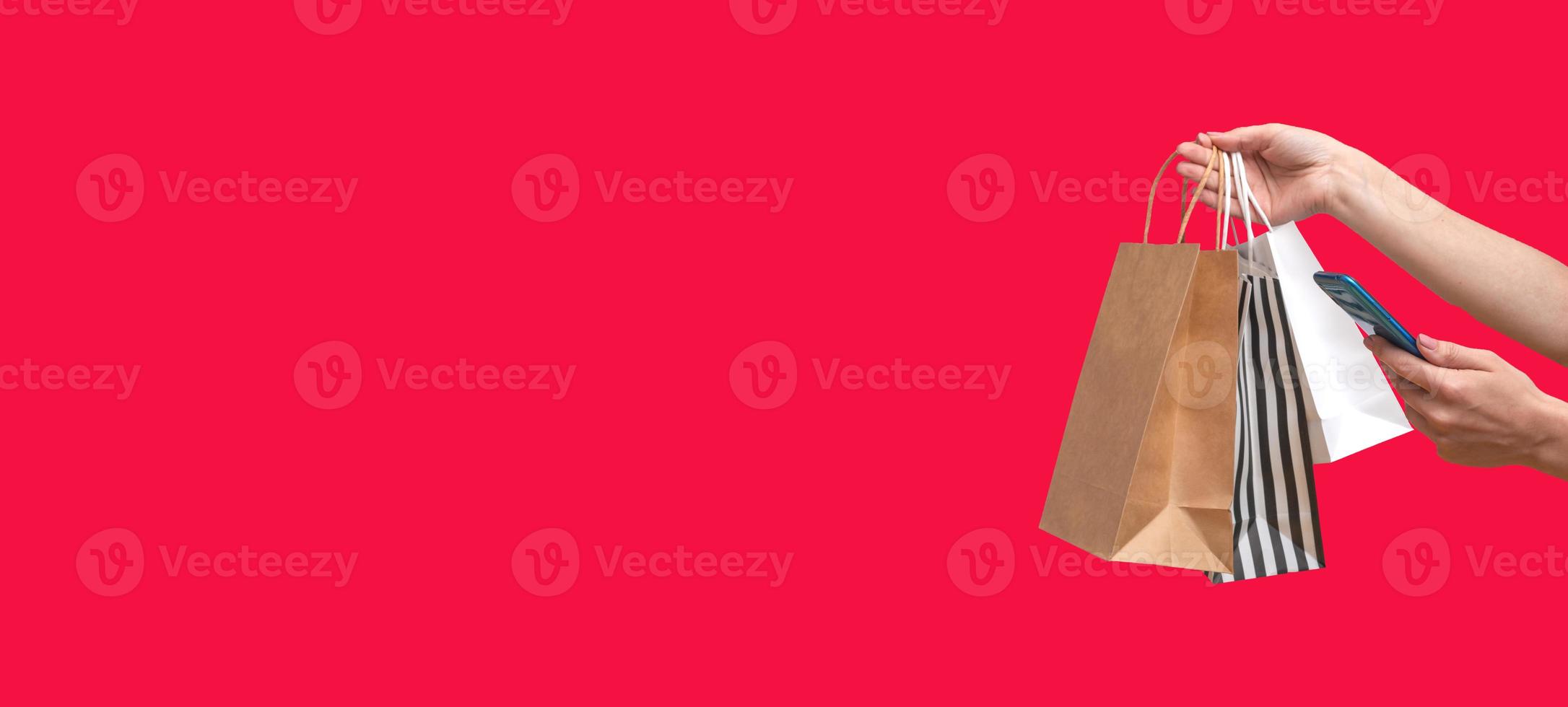 Woman shopping online from a mobile phone. Female hands with packages isolated on red background, copy space. Banner photo