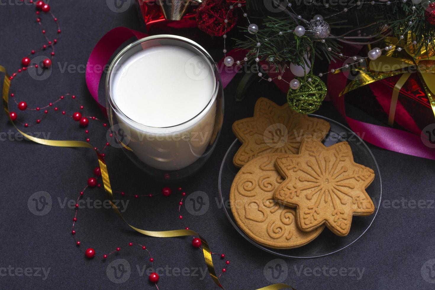 pan de jengibre y leche para santa. Composición navideña con galletas de jengibre y leche sobre un fondo negro con un árbol de navidad y un regalo. foto