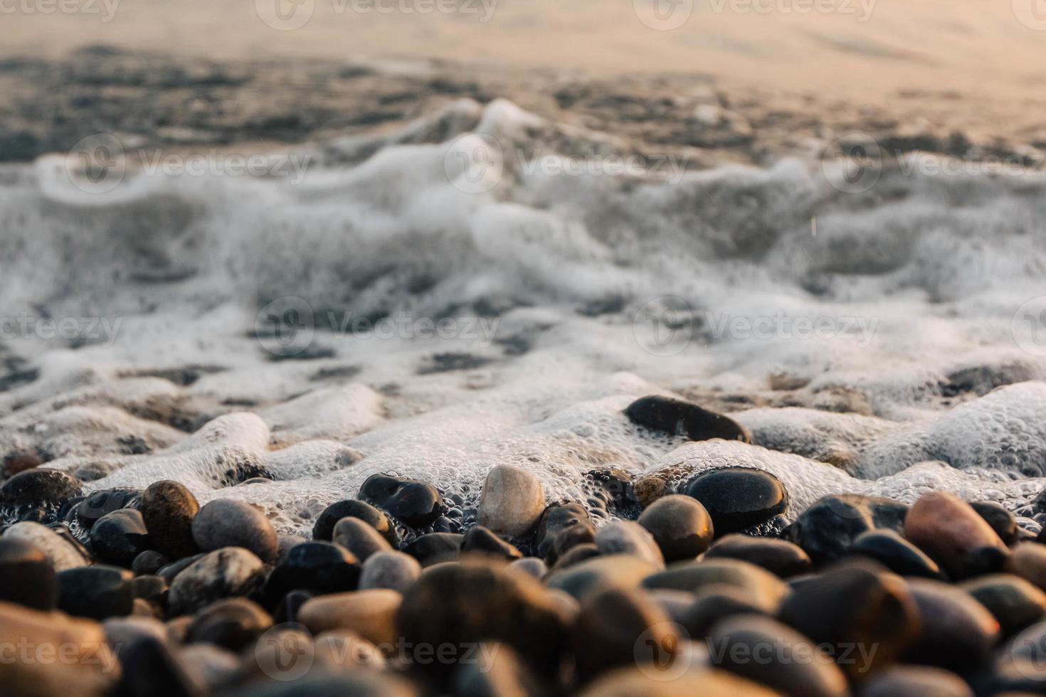 pequeñas piedras junto al mar con efecto bokeh. fondo decorativo borroso, lugar para el texto. papel tapiz de verano, luz del atardecer soleado foto