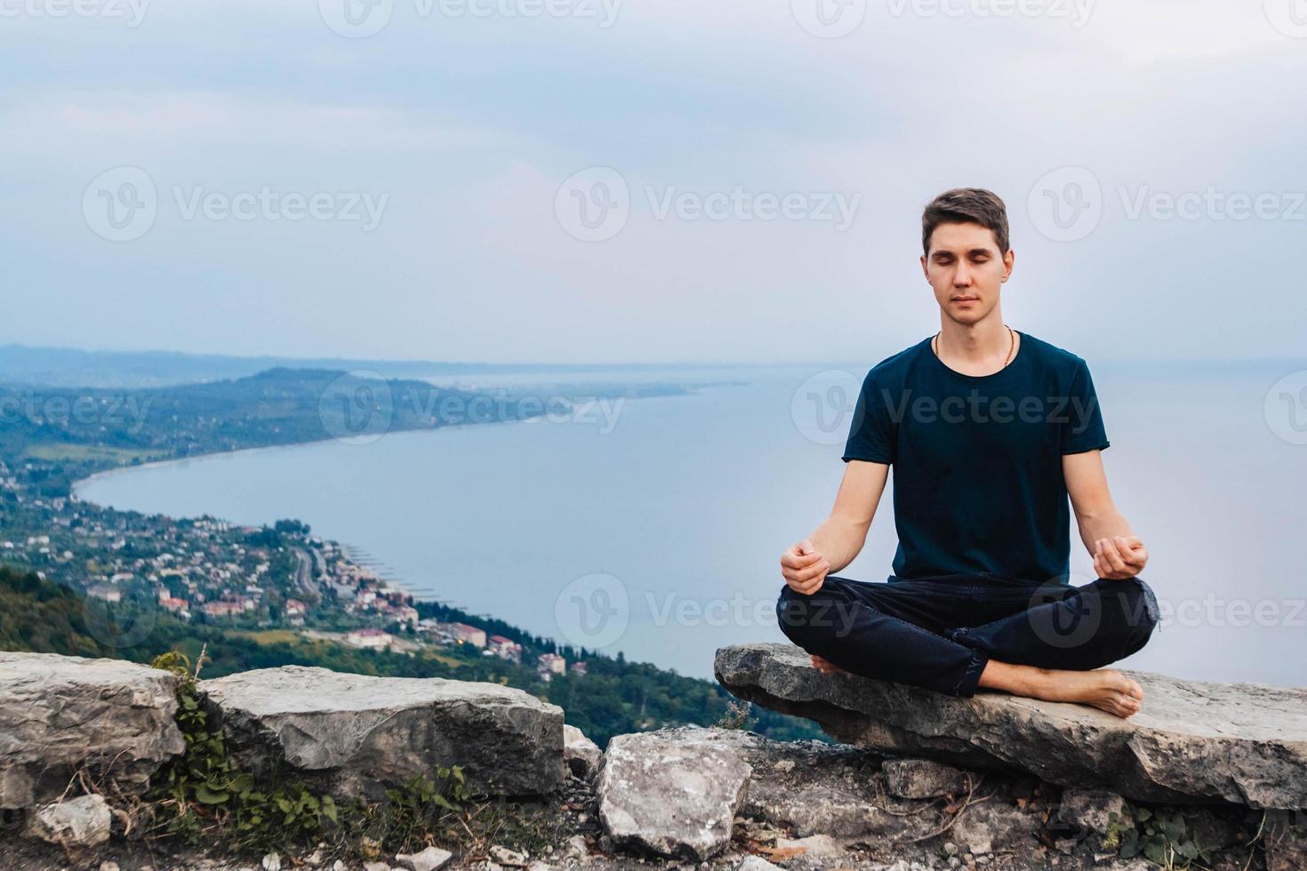 El hombre en una posición meditativa se sienta en un césped sobre un fondo de bosque y puesta de sol foto