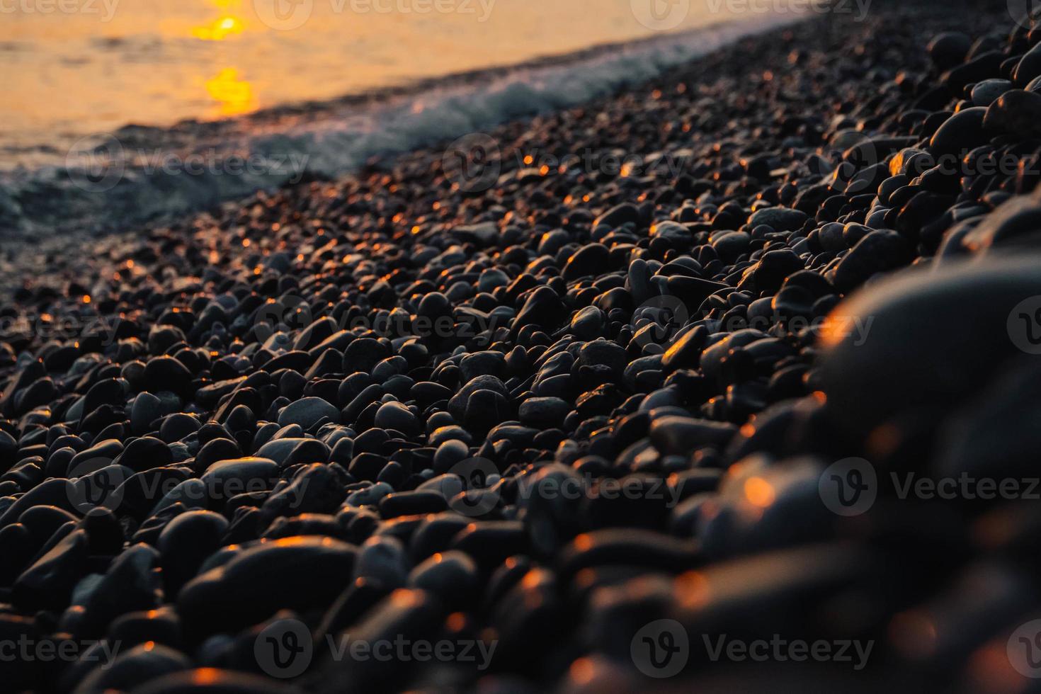 pequeñas piedras junto al mar con efecto bokeh. fondo decorativo borroso, lugar para el texto. papel tapiz de verano, luz del atardecer soleado foto