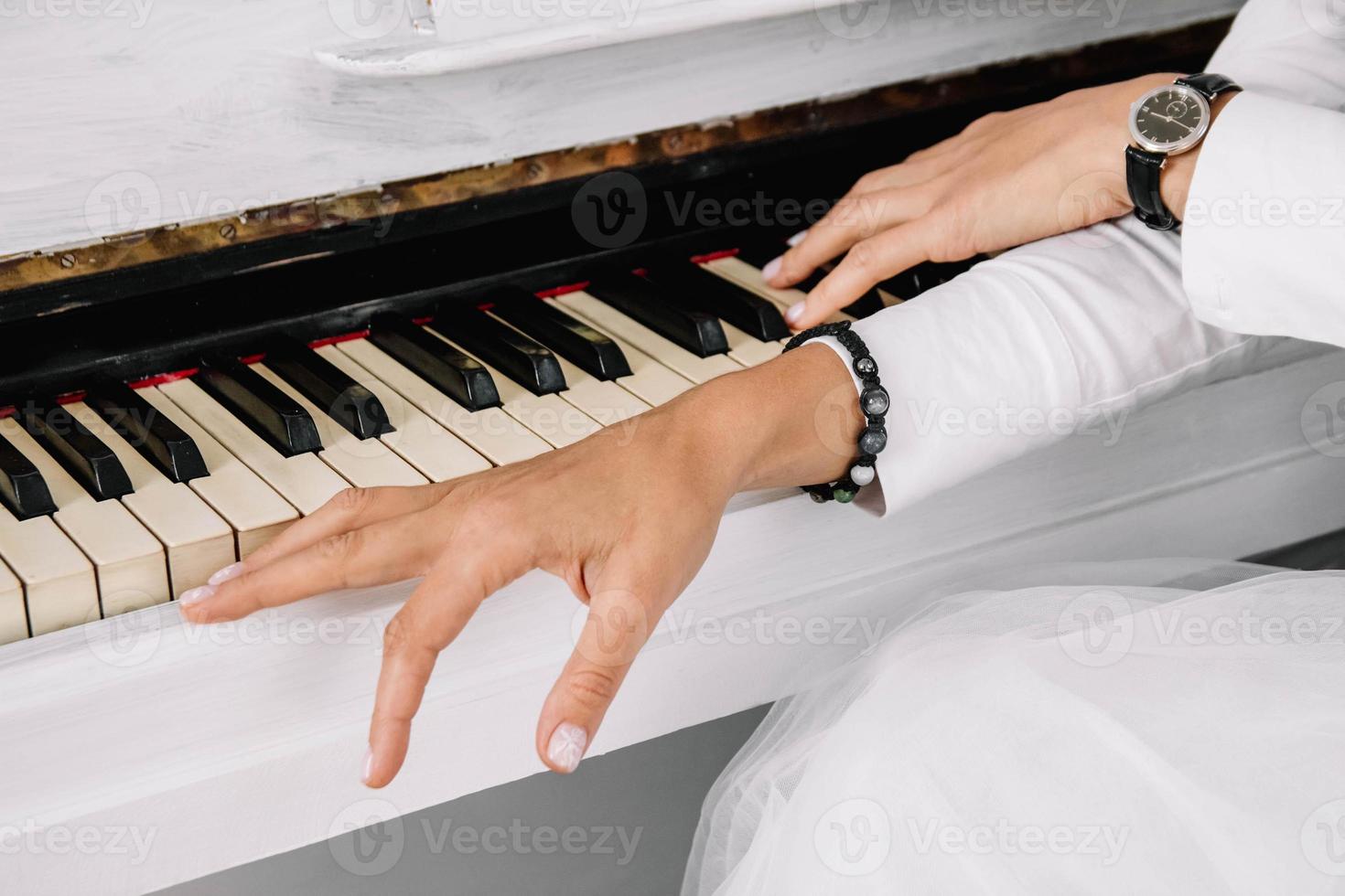 Manos de mujer vestida con ropa blanca tocando el piano blanco foto