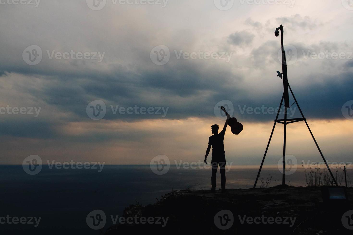 Silhouette of a man holding a guitar on a background of clouds and sea photo