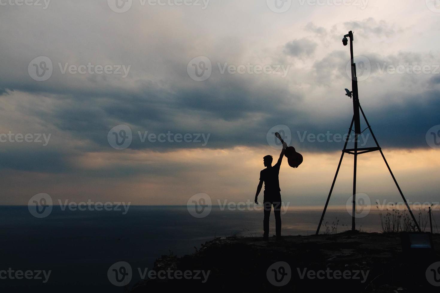 silueta de un hombre sosteniendo una guitarra sobre un fondo de nubes y mar foto