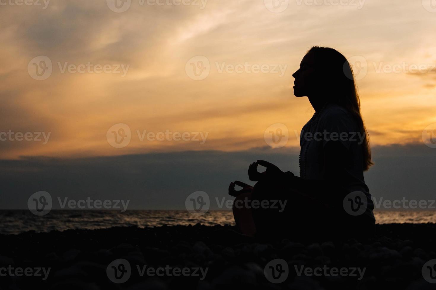 Silueta de una mujer en pose de meditación en la playa durante la puesta de sol surrealista en el fondo del mar y el cielo dramático foto