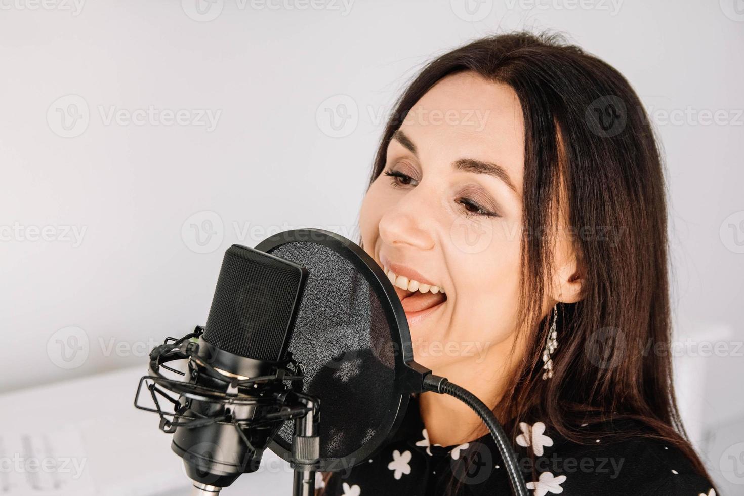 Portrait of beautiful woman sings a song near a microphone in a recording studio. Place for text or advertising photo