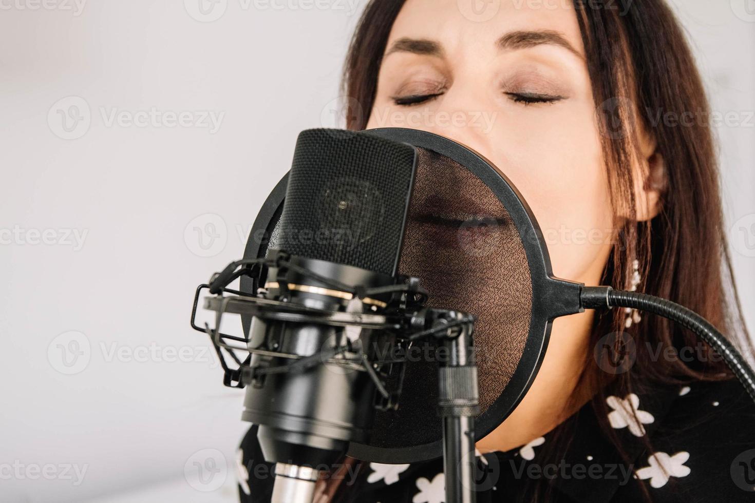 Portrait of beautiful woman sings a song near a microphone in a recording studio. Close-up face photo