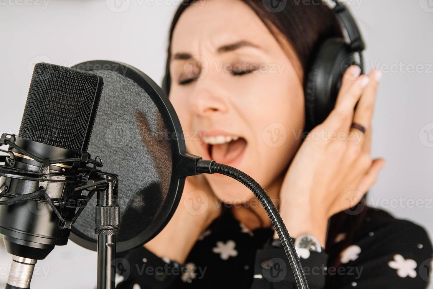 Beautiful woman in headphones sings a song near a microphone in a recording studio. Place for text or advertising photo