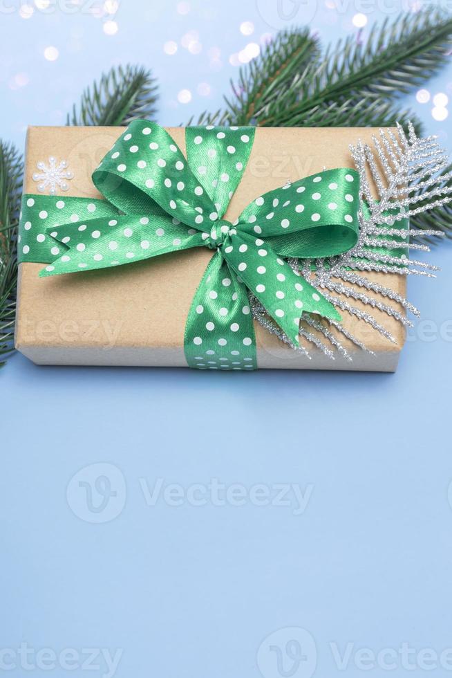 Feliz navidad y próspero año nuevo. regalo con una cinta verde con lunares y adornos sobre un fondo azul con luces. espacio de copia de tarjeta navideña de cerca. vertical foto