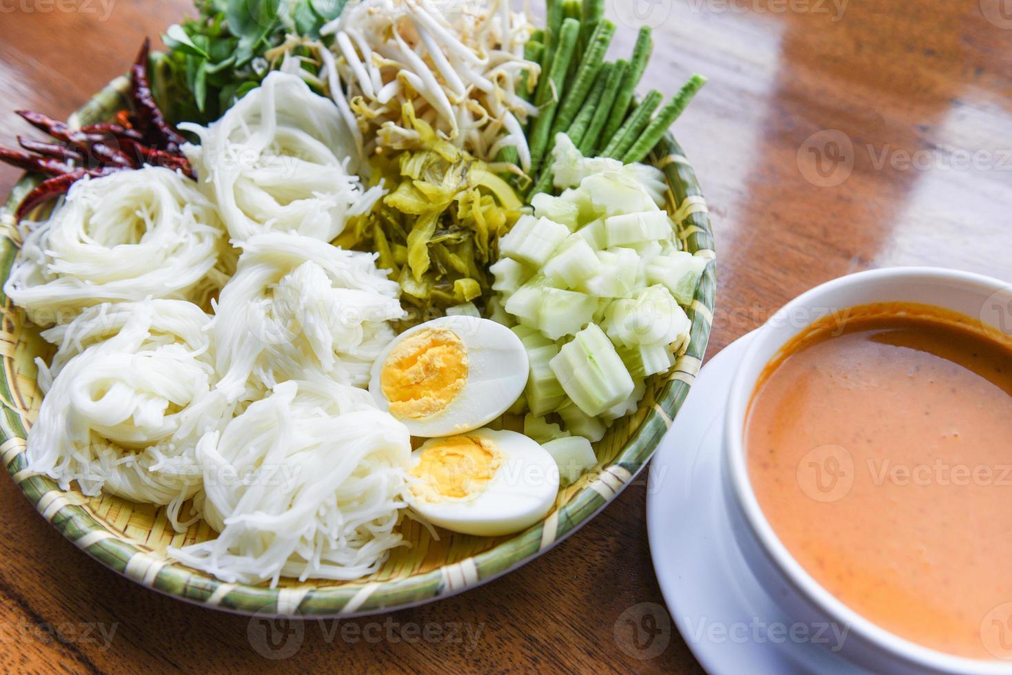 Thailand food vermicelli noodle boiled eggs and fresh vegetables on plate with curry soup bowl served wooden table - Thai rice noodles photo