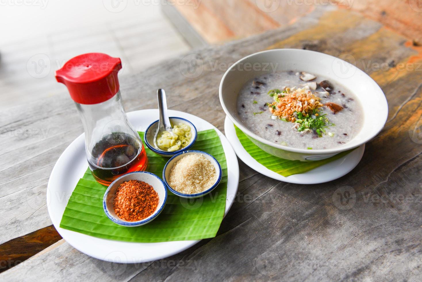 Gachas de arroz o papilla - arroz hervido con setas shiitake de cerdo y verduras con salsa de condimentos en la mesa de madera foto