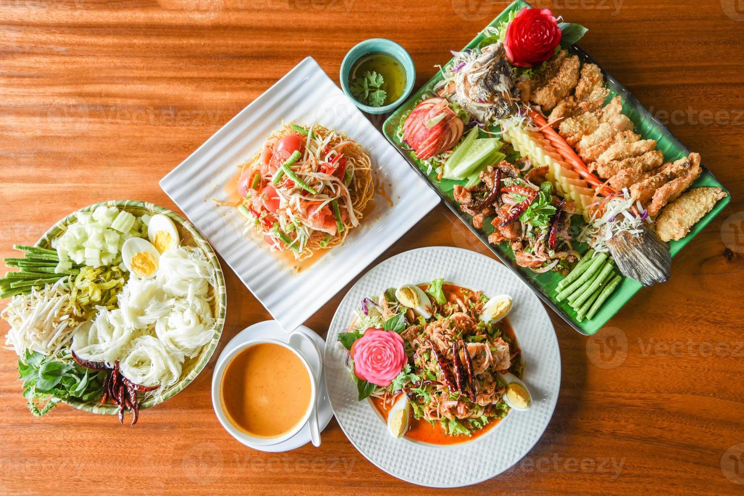 Asian Thai food top view with Thai rice noodles curry , Papaya salad , shrimp salad and Salad fish food served on wooden table setting plate photo