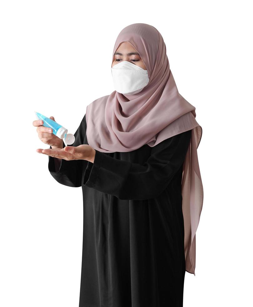 Muslim woman wearing a surgical mask washing hands with alcohol gel on white background. Covid-19 coronavirus concept. photo