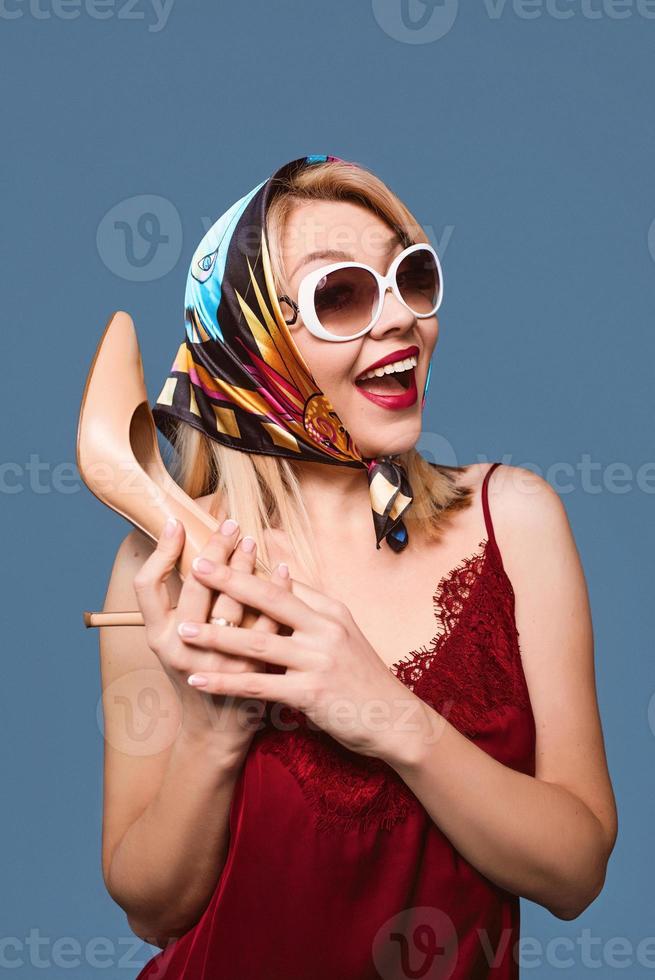 Divertido elegante sonriente alegre elegante mujer rubia con maquillaje y con zapato de tacón en sus brazos y bandera italiana en el fondo foto