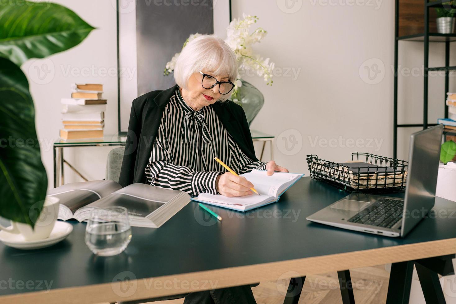 Mujer de cabello gris hermoso senior agua potable durante el trabajo en la oficina. trabajo, personas mayores, equilibrio hídrico, encontrar una solución, concepto de experiencia foto