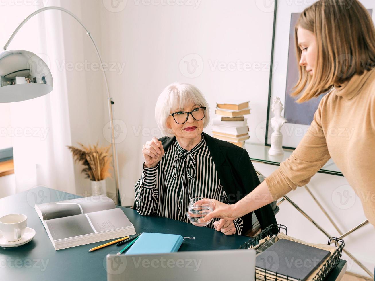 mujer con estilo senior con mujer joven discutiendo las tareas laborales en la oficina. negocio, comunicación, trabajo, edades, colaboración, concepto de tutoría foto