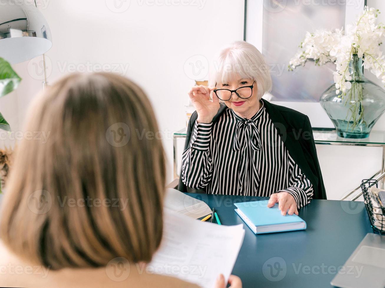 senior stylish woman with young woman discussing work tasks in office. Business, communication, work, ages, collaboration, mentoring concept photo