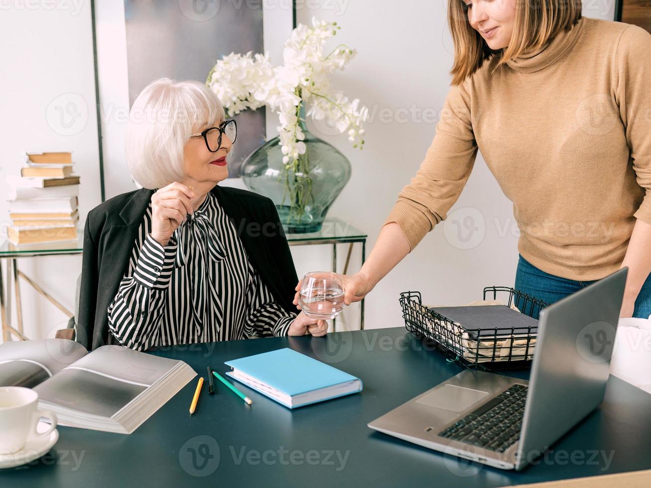 young assistant brought a glass of water to the boss in office. Business, communication, work, ages, collaboration, mentoring concept photo