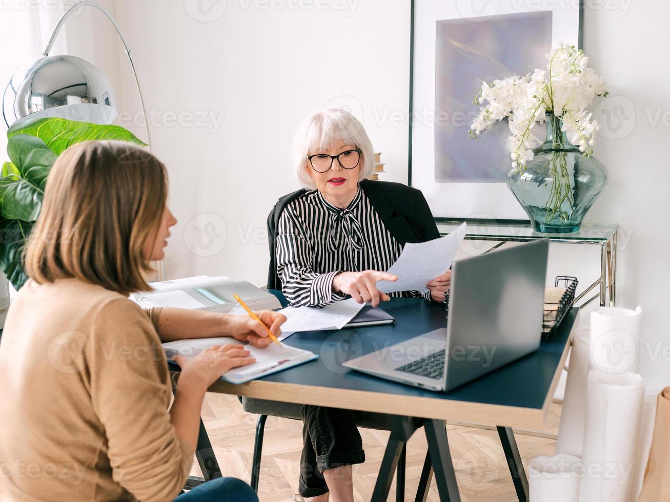 mujer con estilo senior con mujer joven discutiendo las tareas laborales en la oficina. negocio, comunicación, trabajo, edades, colaboración, concepto de tutoría foto