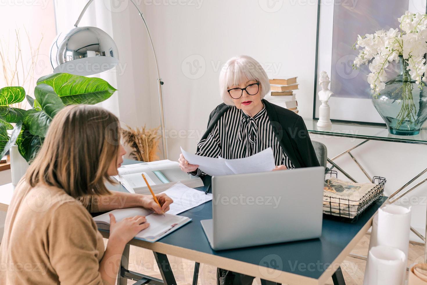 mujer con estilo senior con mujer joven discutiendo las tareas laborales en la oficina. negocio, comunicación, trabajo, edades, colaboración, concepto de tutoría foto